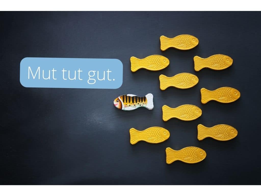 alt=„9 gelbe Fische schwimmen nach rechts, ein bunt gemusterter Fisch schwimmt nach links“